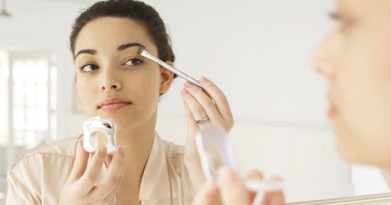 Young woman applying make-up in mirror, using brush, close-up