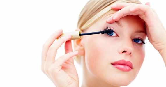 Closeup of cute female applying mascara with brush on white back